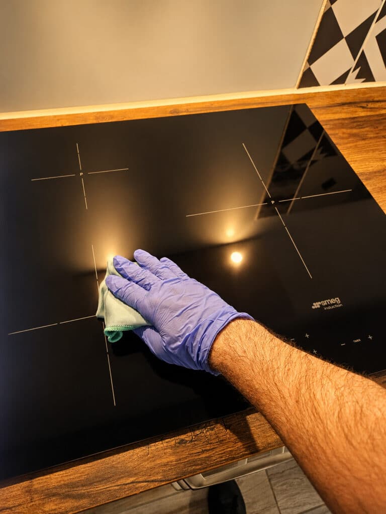 Main gantée nettoyant une plaque induction noire avec chiffon microfibre dans une cuisine moderne