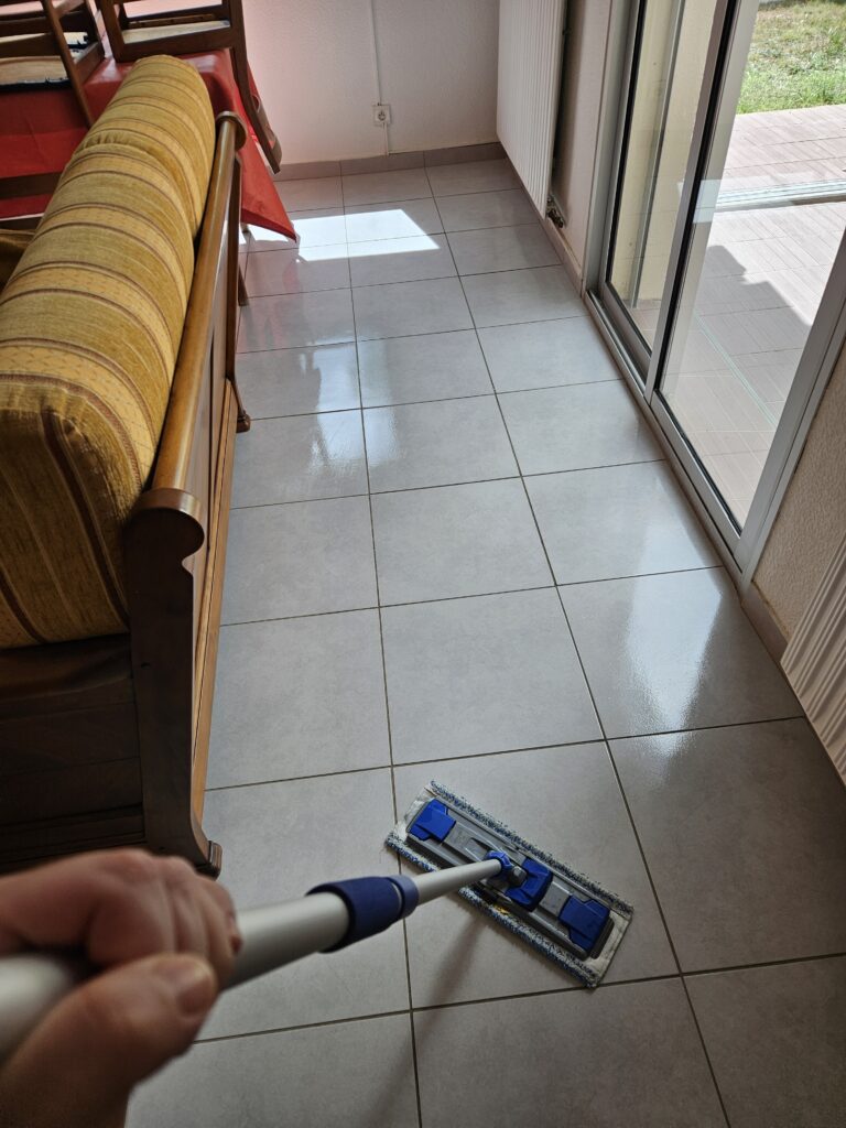 Étienne lave un sol carrelé avec un balai microfibre lors d’une intervention à domicile