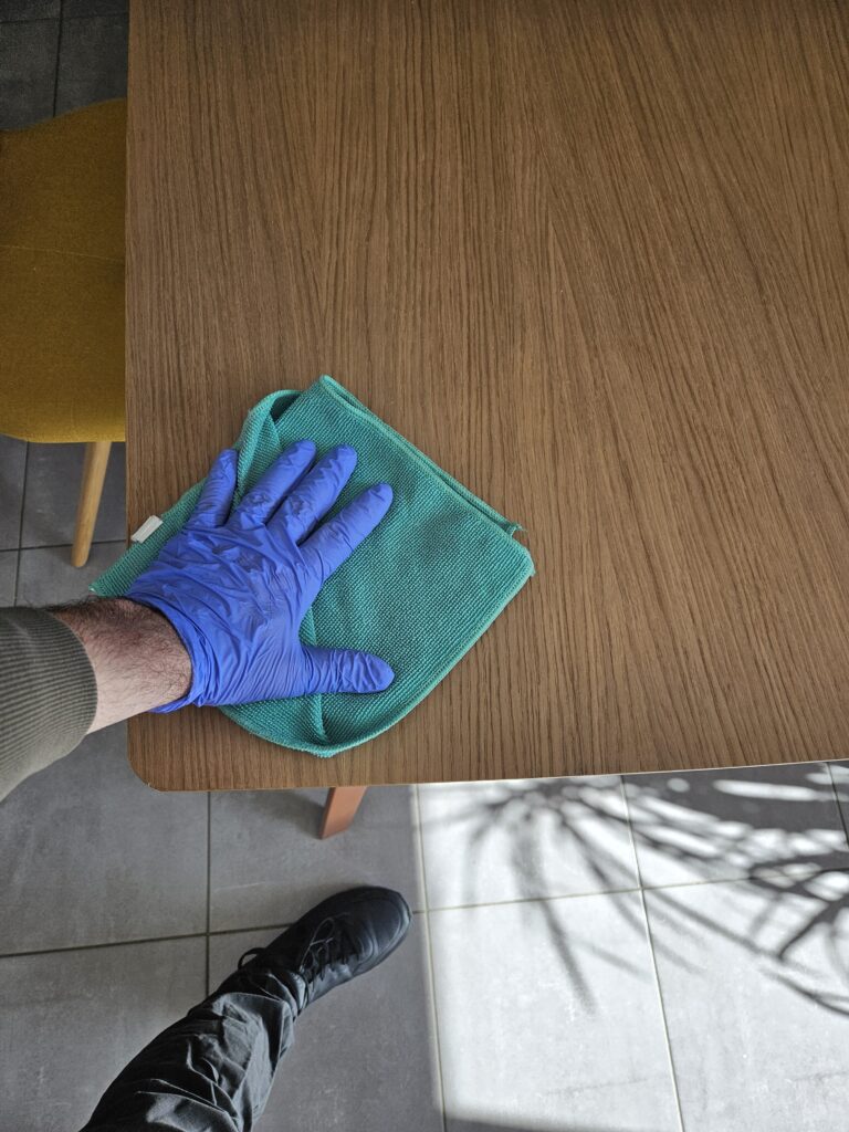 Main gantée d’Étienne nettoyant une table en bois avec une microfibre