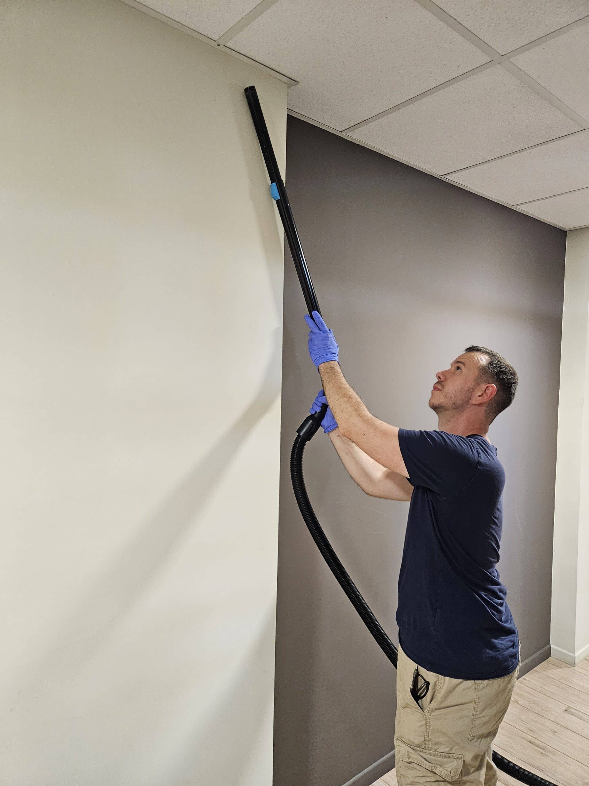 Étienne nettoie les parties hautes d’un logement à l’aide d’un aspirateur
